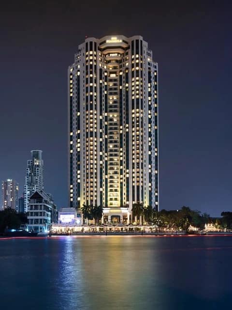 The Peninsula Bangkok tower lit up over the river at night